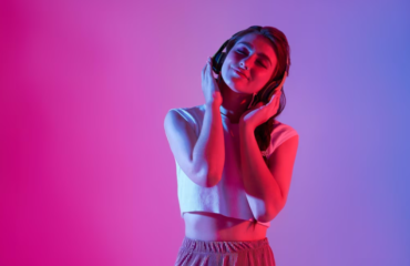 Woman in wireless headphones listening to songs with closed eyes under neon light